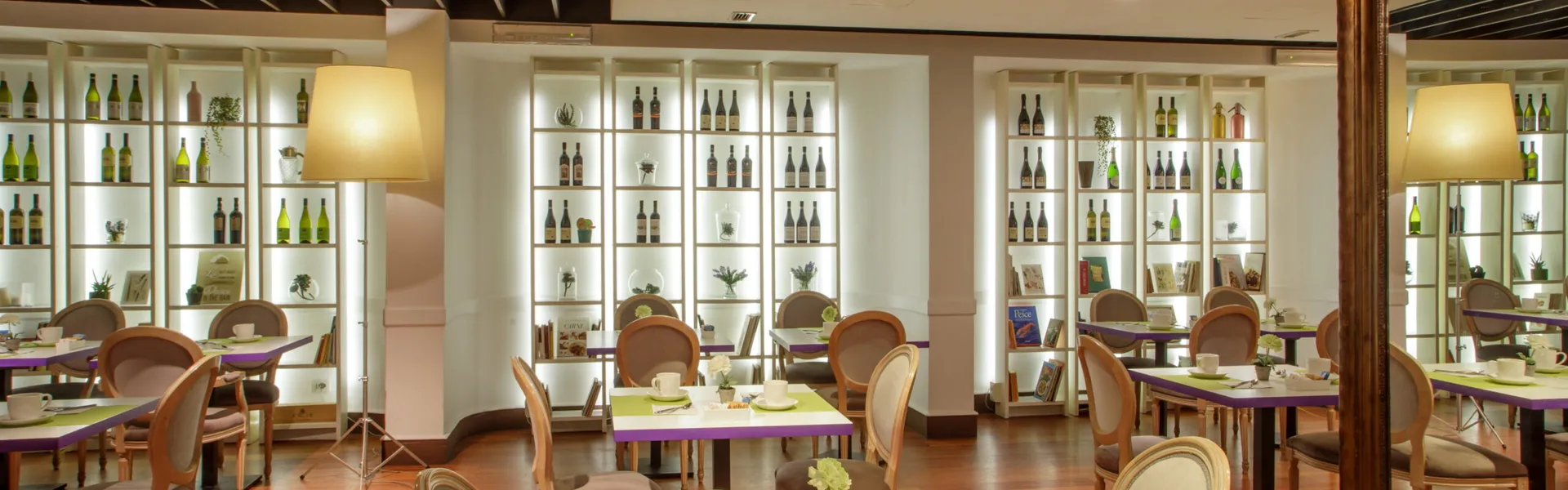 La sala del ristorante del Fenix Hotel Roma con i tavoli apparecchiati e le librerie di bottiglie illuminate